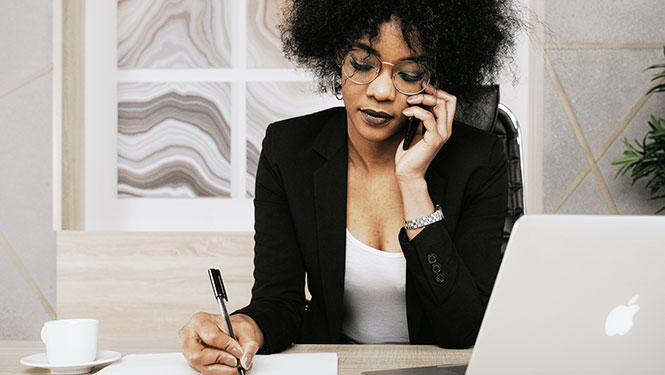 A women at work in an office taking notes while talking on the phone