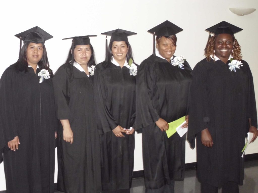 Five DLC graduate women wearing their caps and gowns and smiling together